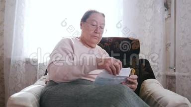 一位老妇人坐在椅子上，在窗户的背景上打开一封信。